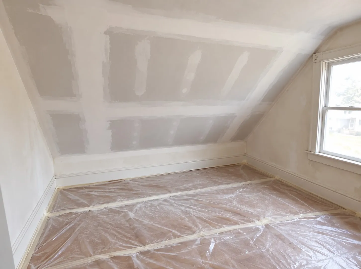 Ceiling repair in progress: replaced drywall on a sloped ceiling, seams taped and first-coated, floor covered in plastic