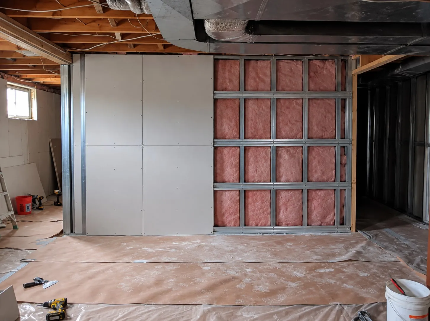 Basement soundproofing in progress: drywall on half the wall, the other half open to insulated metal studs crossed by resilient channel