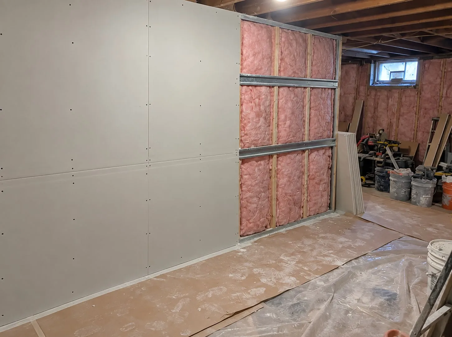 Basement wall partway through a soundproofing job: drywall screwed over metal channel on half the wall, insulated stud bays still open on the rest
