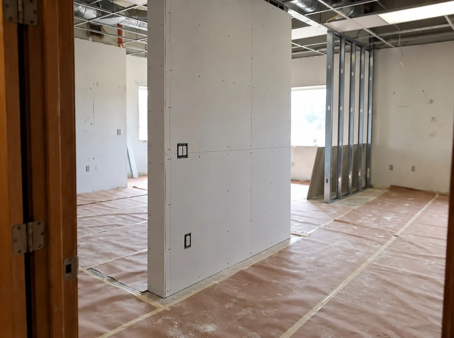 Commercial build-out in progress: a new drywall partition with outlets in place and a bare metal-stud wall framed behind it under the ceiling grid